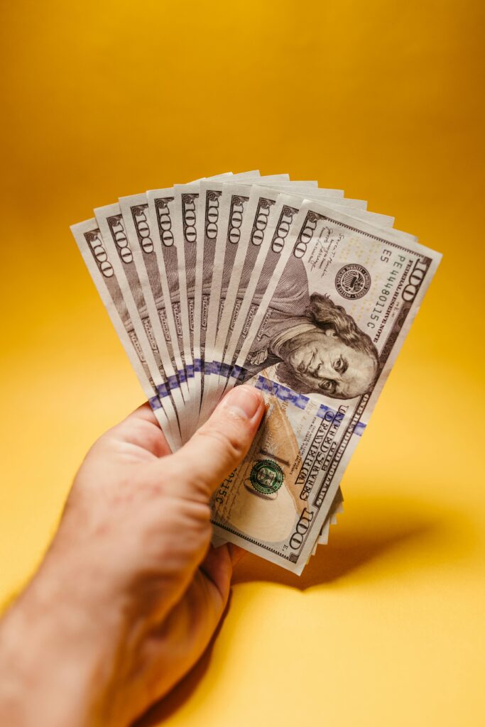 Close-up of a hand displaying US dollar bills against a bright yellow backdrop, signifying wealth and finance.